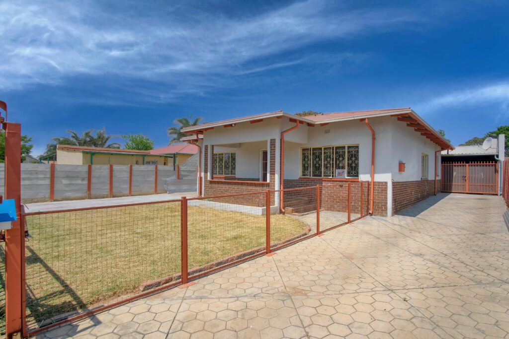 Exterior view of a suburban house with a fenced yard in Pretoria, South Africa, under a clear summer sky.